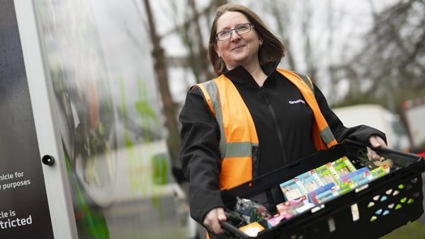 A woman in a high vis vest carries a container of packaged sandwiches