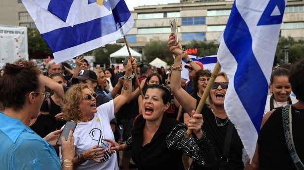Men and women look happy as they wave white and blue Israeli flags in an outdoor area