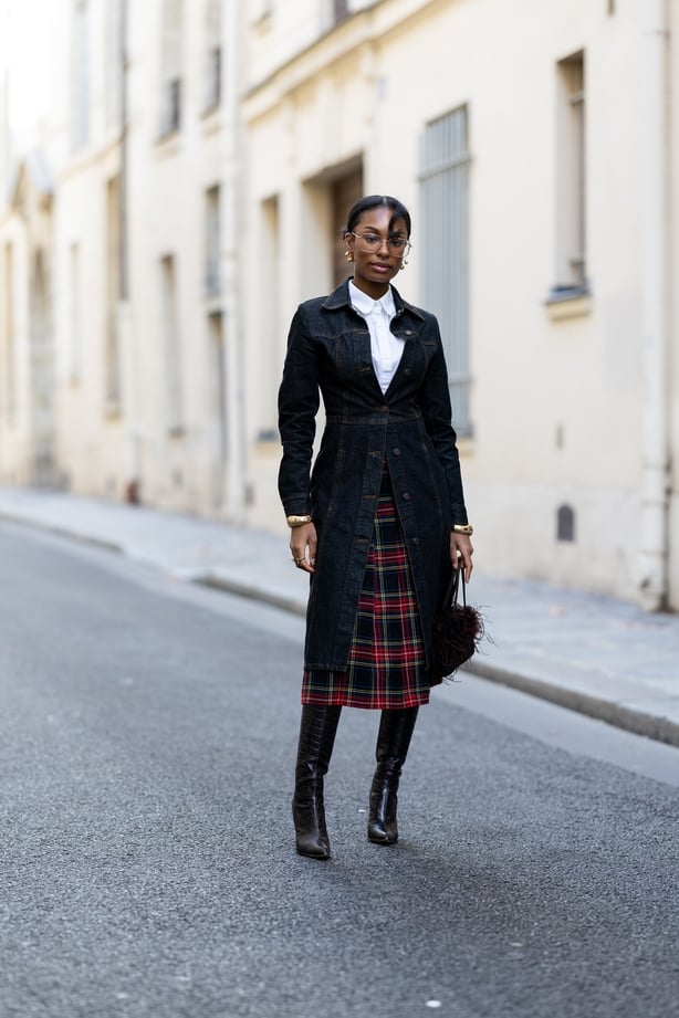 A guest wears dark brown leather heeled knee high boots, a denim long jacket, a white shirt, a black bag to Paris Fashion Week 2025 