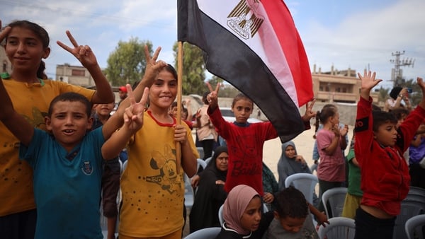 Several Palestinian children wearing colourful clothes look happy as they wave a red, white and black flag in an outdoor area