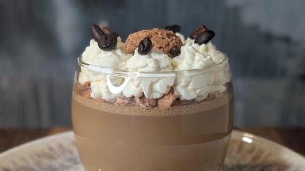 A chocolate dessert topped with cream, coffee beans and biscotti