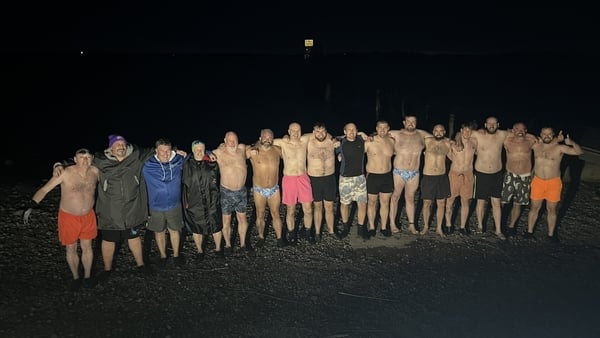 A group of men lined up arm in arm on a beach in the dark