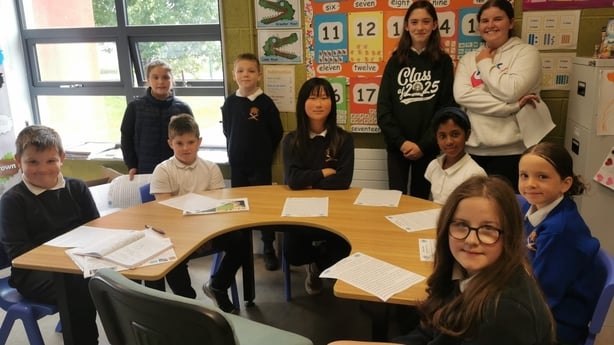 ten children and their teacher sit around a desk in a classroom