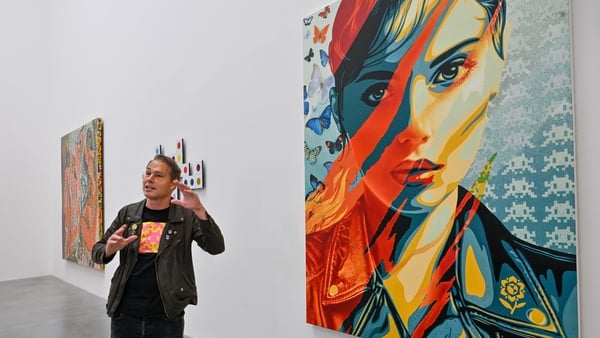 Shepard Fairey is seen giving an interview with his piece Flames of Sicontent, 2025 hanging behind him