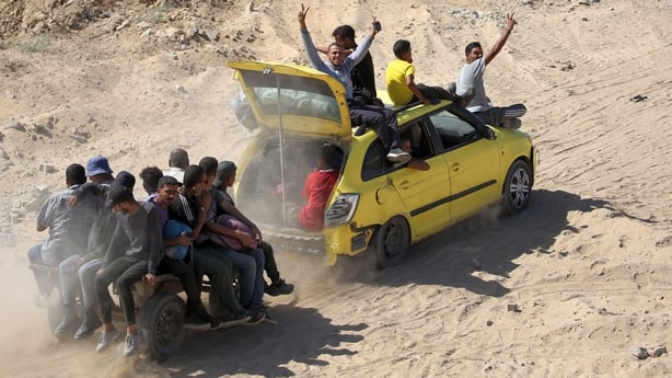 Men gesture as they sit atop a vehicle towing another cart with passengers aboard moving along a dirt road to Gaza City 