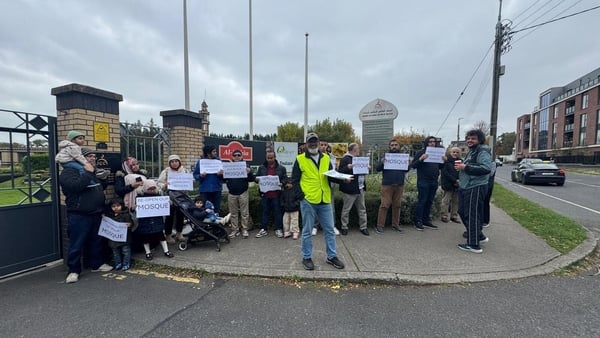 A group of people, including young children, protest outside a mosque in Dublin and hold signs calling for it to reopen