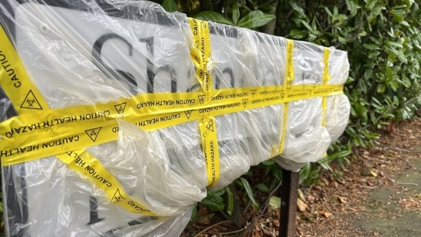 A street sign is wrapped in plastic with yellow tape around it after it was damaged