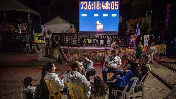 People sit and talk in front of a clock counting the days the hostages have been in captivity at Hostages Square