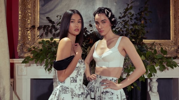 Two models posing in front of a large painting and floral arrangements