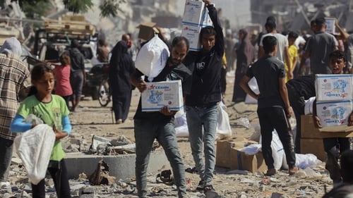People walk through a heavily damaged street in Khan Younis carrying boxes of aid supplies