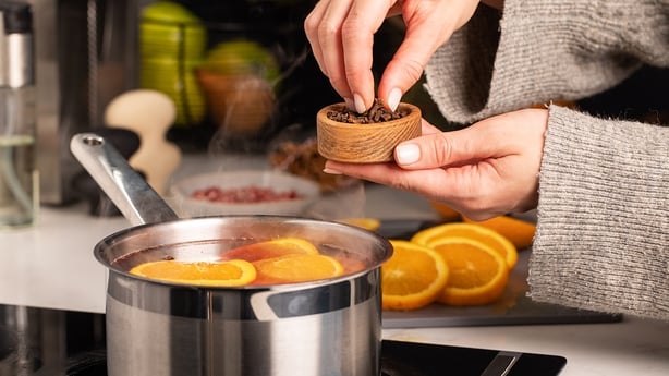 A woman adds cloves to the boiling mulled wine in a saucepan in the kitchen. 
