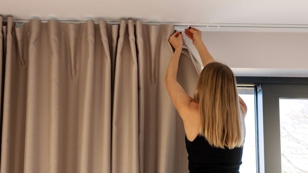 woman hanging window curtains at home
