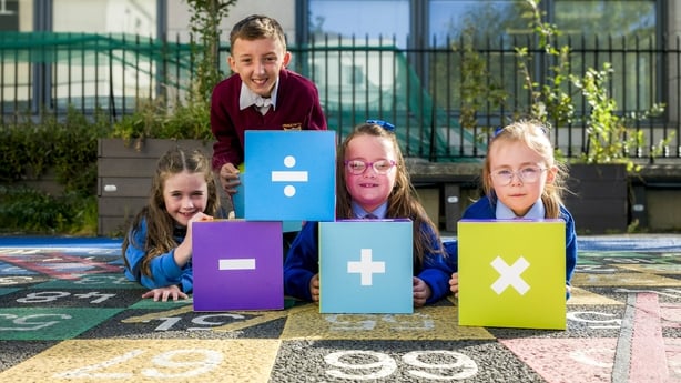Children pose in front of cubes faeturing maths symbols.