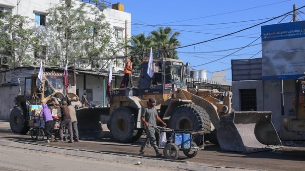 Palestinians walks past bulldozers the Gaza Municipality prepared to deploy to clear building rubble from main axes and streets in Gaza City