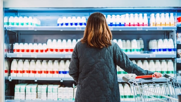 Rear view shot of a female customer looking and choosing fresh bottled milk while standing in front of a display fridge full of diary products in supermarket.
