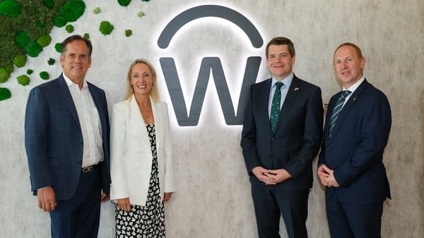 Image of three men and a woman in suits in front of the Workday logo