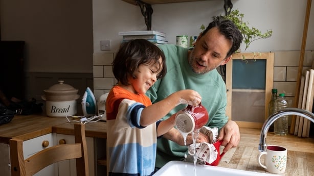 A waist-up shot of a male child and his dad washing and drying dishes together