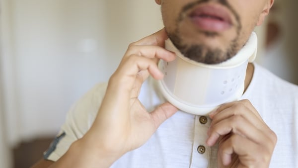 Close-up of a man adjusting his cervical collar neck brace while seated at a wooden table
