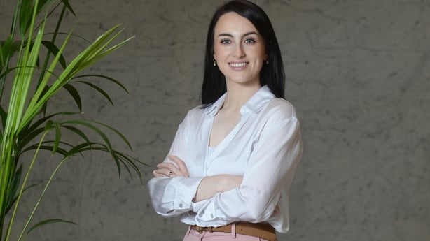 Leah McMahon of Castle Capital stands with arms folderd beside a plant