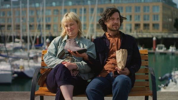 A woman and man sit on a bench at a pier.
