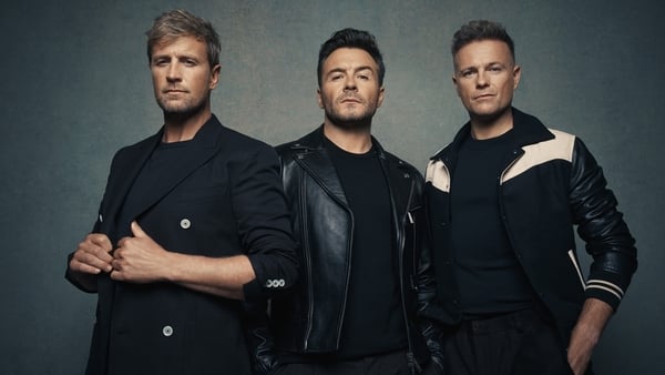 Westlife, dressed in black, posing against a plain backdrop.