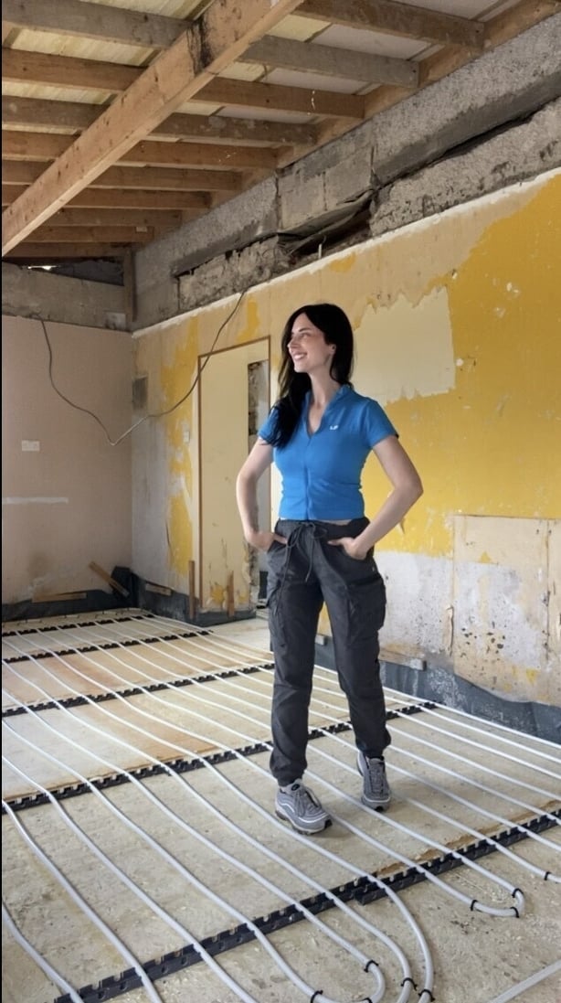 A woman standing in a room being renovated with exposed underfloor heating