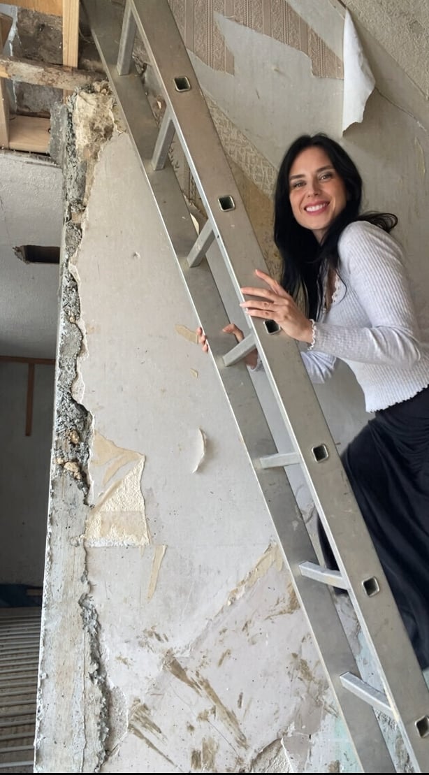A woman standing on a ladder beside a cracked plaster wall