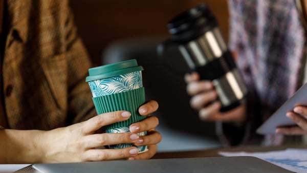 Close up shot of two unrecognisable businesswomen sitting at desk in a modern office space, engaging in casual conversation over cups of coffee during office break.