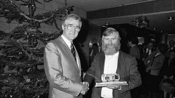 John Sheahan, Composer and member of The Dubliners who Composed the song "The Marino Waltz", being presented with a Peat Briquette with a picture of O'Donoghues Pub on it by Eddie O'Connor, Managing Director of Bord na Mona in the offices in Baggot Street in Dublin, 17/12/1987 (Part of the Independe