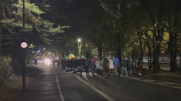 A small group marches at night on road surrounded by trees