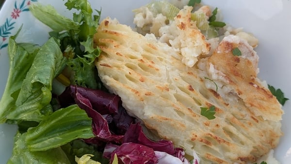 A photo of fish pie with mashed potato on top, beside a colourful salad
