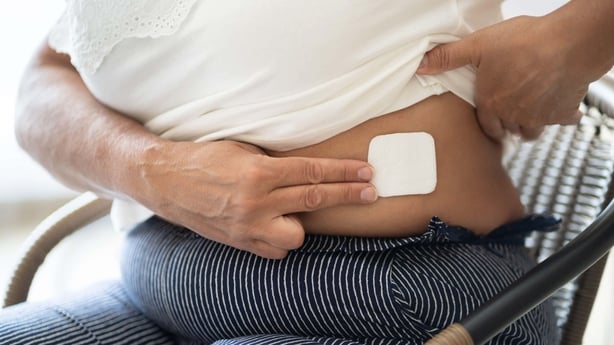A woman lifting her t-shirt to show a HRT patch on her side