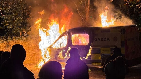 People stand in front of a burning police van
