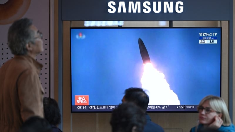 People sit in front of a television screen showing a news broadcast with of a North Korean missile test
