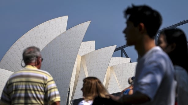Tourists walk in front of the Sydney Opera House