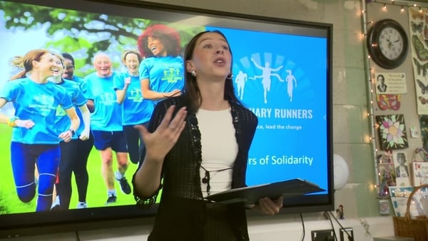 A woman speaking in a classroom in front of a projector screen.