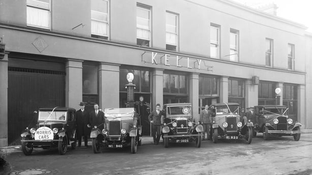 Black and white photo of men in suits standing with Morris cars