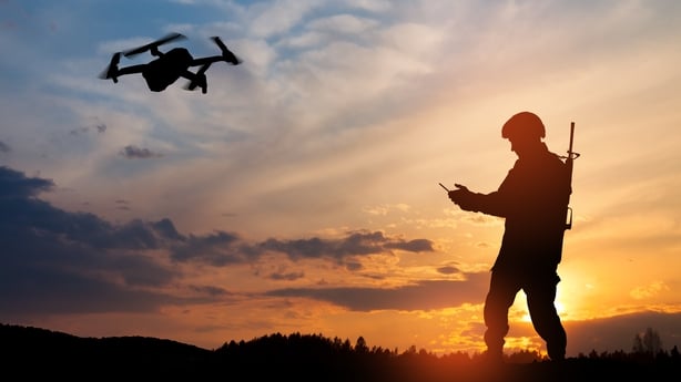 Silhouette of a soldier using a drone and laptop computer against the backdrop of a sunset.