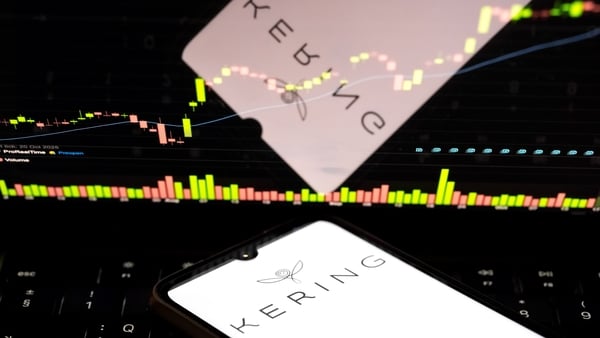 The Kering logo on a smartphone screen in front of a stock exchange curve chart