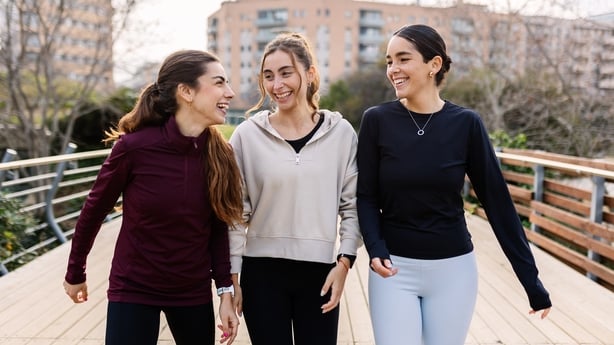 Three athletic young women are enjoying a walk together after their workout, sharing laughter and conversation on a wooden bridge