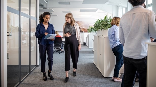 Businesswoman discussing with pregnant colleague over document while walking in creative office