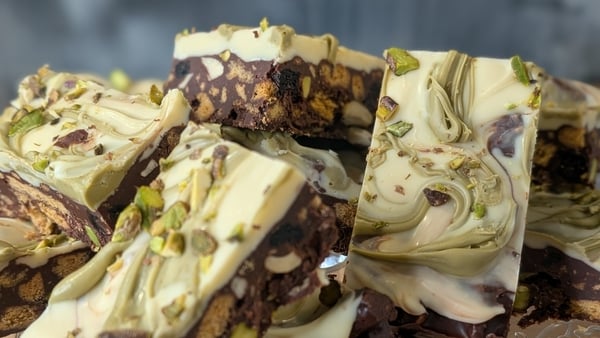 A plate of chocolate tiffin with fruits and nuts in them, topped with white chocolate and swirls of pistachio cream