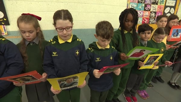 Children stand in a line in a classroom reading a presentation.