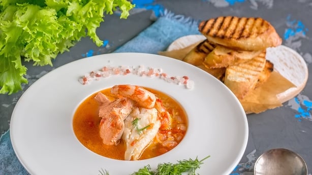 French fish soup Bouillabaisse with seafood, salmon fillet, shrimp, rich flavor, delicious dinner in a white beautiful plate.
