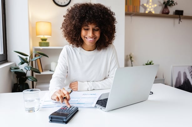 Young woman is smiling while using a calculator and laptop for her home finances