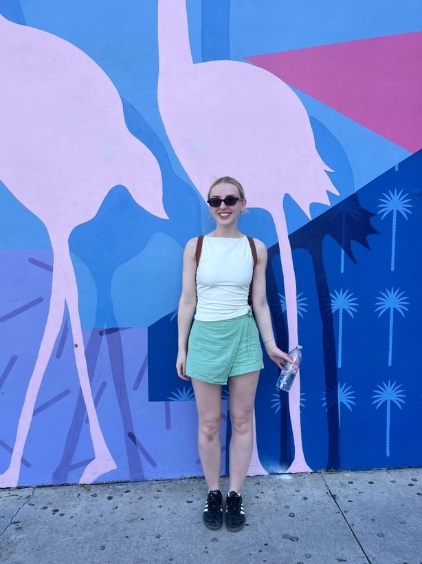A blonde woman smiling for a photo in front of a mural