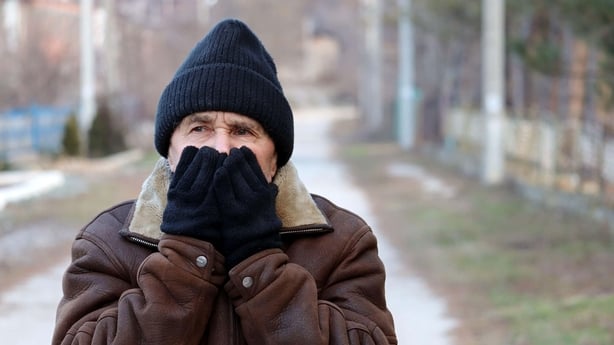 An older man covering his face with his hands while out in the cold