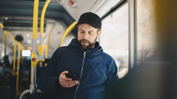 A man wearing a blue jacket and a black hat using his phone on public transport A man wearing a blue jacket and a black hat using his phone on public transport