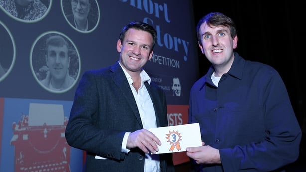 judge Tristan Rosenstock presents Ian Feighery with 3rd prize in the 2025 RTÉ Short Story Competition, on stage at awards night in Pavilion Theatre Dun Laoghaire