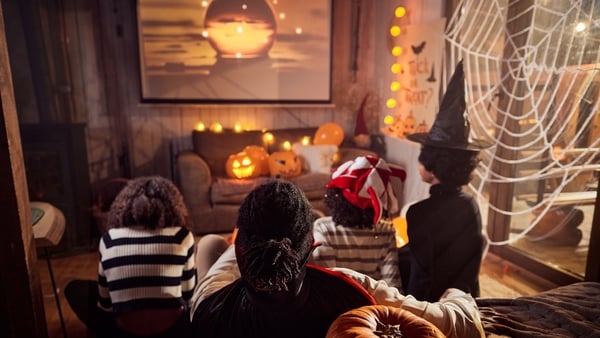 Back view of African American parents watching a movie with their kids on TV during Halloween night at home.